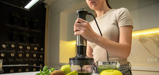 Young woman with electric immersion blender preparing smoothie in kitchen