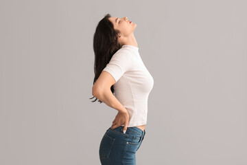 Beautiful young woman suffering from back pain on grey background
