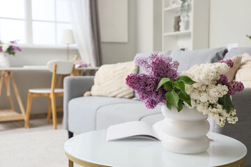 Vase with lilac flowers and magazine on table in living room, closeup