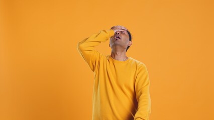 Fototapeta premium Delivery man doing face palm after realizing he forgot to put orders in thermal backpack. Upset courier making mistake, failing to remember to put lunch boxes in bag, studio background, camera B