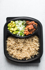 Overhead view of rice mackerel bowl in a takeaway plate, top view of healthy rice bowl meal prep, basmati rice mackerel avocado and cucumbers in a black disposable plastic plate