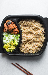 Overhead view of rice mackerel bowl in a takeaway plate, top view of healthy rice bowl meal prep, basmati rice mackerel avocado and cucumbers in a black disposable plastic plate