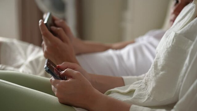Cropped shot of young couple together quickly clicking fingers smartphones screen to farming new popular Hamster Kombat cryptocurrency in mobile phone online application, sitting on sofa, slow motion.