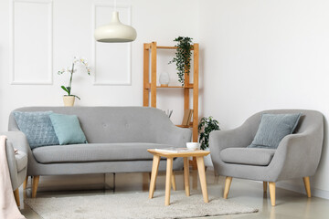 Interior of light living room with grey sofa, cozy armchair and coffee table