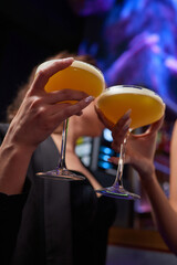 A woman holds a cocktail in her hand, with her fingers wrapped around the glass