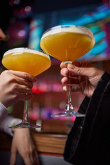 Two friends lifting cocktails in a lively bar scene, expressing joy and celebration