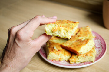 Close up of a hand holding a piece of homemade zucchini pie and a plate with other pieces in the background