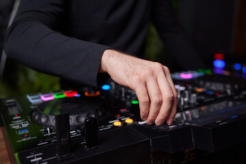 control DJ for mixing music with blurred people dancing at party in nightclub.