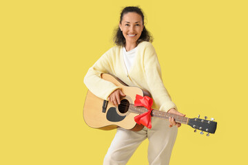 Fototapeta premium Mature woman with gift guitar on yellow background