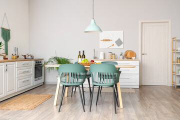 Interior of modern kitchen with dining table, chairs, white counters and lamp