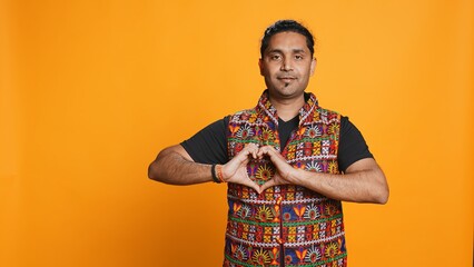 Portrait of smiling loving man doing heart symbol shape gesture with hands, showing kindness. Happy affectionate person doing tender love gesturing, isolated over studio background, camera B