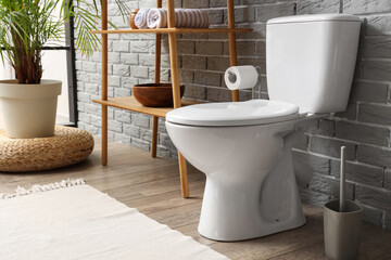 Interior of restroom with toilet bowl, plant and shelving unit near grey brick wall