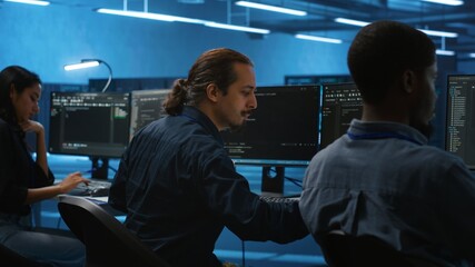 Multiracial coworkers in data center coding and checking parameters on computer. Multiethnic team working together, doing programming in high tech workspace, overseeing server clusters