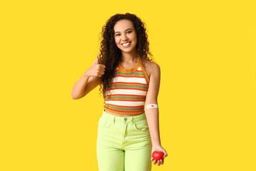 Young female African-American blood donor with applied medical patch and heart showing thumb-up...