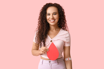 Young female African-American donor with applied medical patch and paper blood drop on pink...