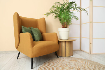 Interior of room with folding screen, armchair and houseplant near beige wall
