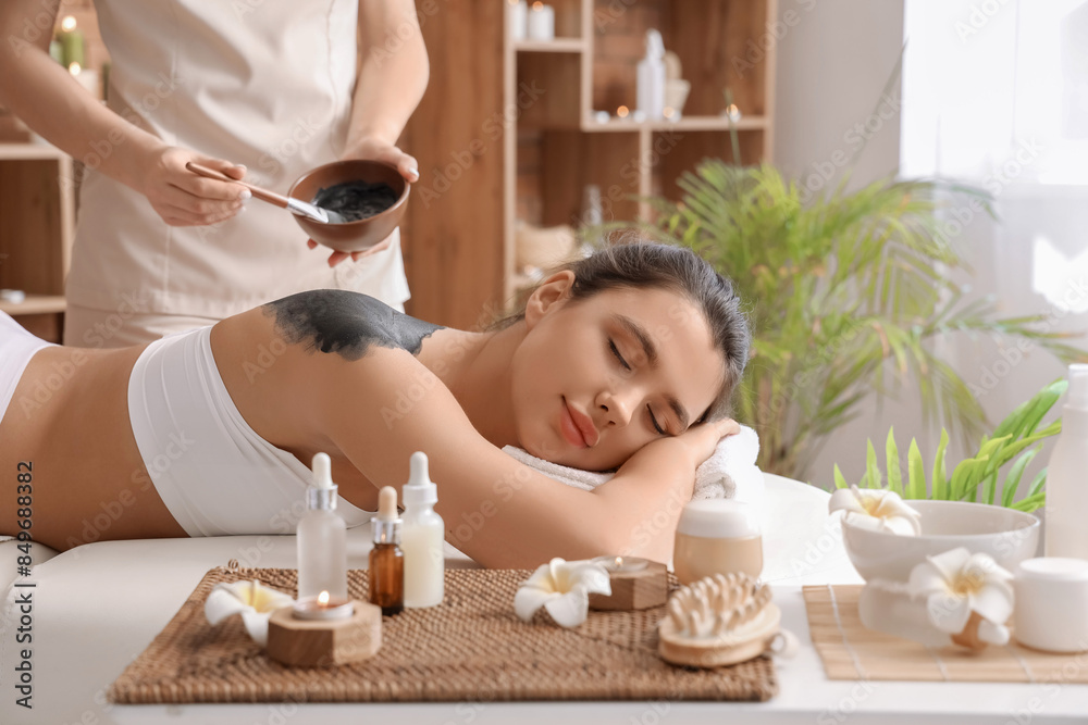 Wall mural young woman undergoing mud treatment in spa salon