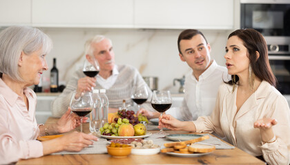 Heartfelt moment as elderly mother and adult daughter enjoying pleasant conversation at family celebration, while men sitting in background with wine