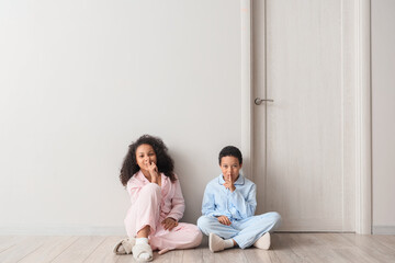 Little African-American children in pajamas showing silence gesture near door at home