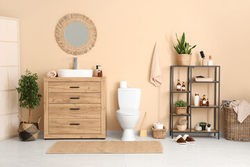 Interior of restroom with sink, toilet bowl and shelving unit near beige wall