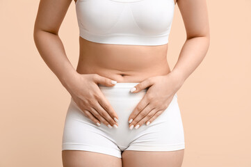 Young woman in underwear suffering from cystitis on beige background, closeup