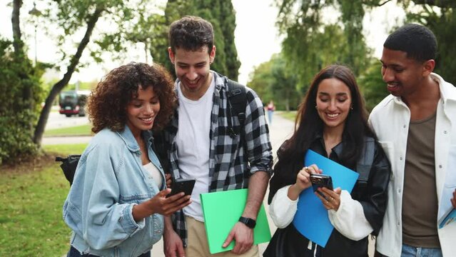 Students socializing and using smartphones in park setting. Diverse students socializing and having fun outdoors in a park setting. Laughter and friendship among college friends
