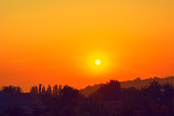 Sunset over rustic hillside with trees in foreground. Serene and picturesque landscape