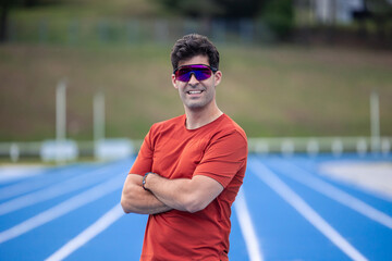 Runner with Sunglasses Smiling at Camera on Blue Athletic Track