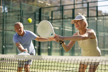Motivated senior man and woman playing padel with his teammate in court