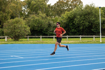 Athletic Man in Orange Shirt and Sunglasses Speedily Running on Blue Athletic Track