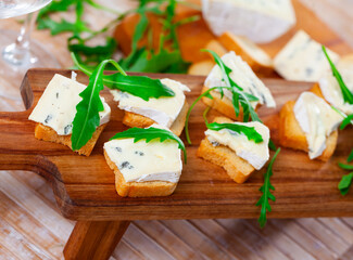 Freshly prepared sandwiches with blue cheese and green arugula on a wooden board