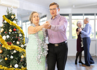 Middle-aged man engaged in modern dance hall with mature female partner and dances Latin rumba...