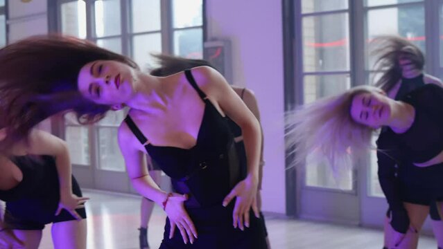 A sexy girl flips her hair towards the camera and dances in front of a group of girls. Heels dance in the evening light.