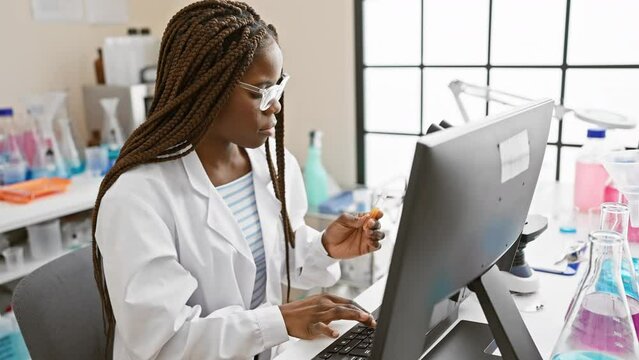 African american scientist woman examining a sample while working with a computer in a laboratory setting.