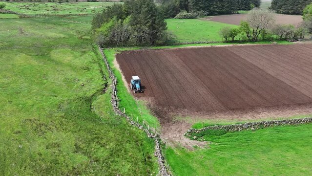 Aerial video of a blue tractor rotovating a field for crops at a farm