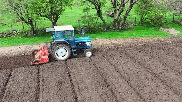 Aerial video of a blue tractor rotovating a field for crops at a farm