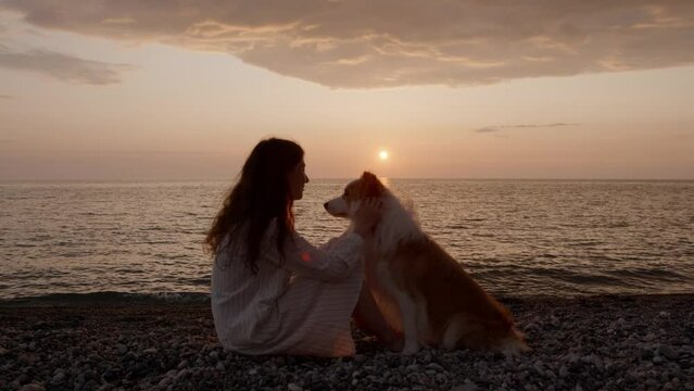 Border collie doggy and woman owner silhouette hug caress each other at the sea beach at beautiful sunset. Spend time together, friendship, vacation concept. Friends forever. Outdoor animal friendship