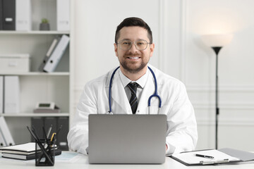 Smiling doctor with laptop at table in clinic. Online consultation