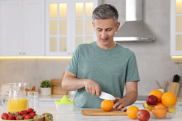 Making juice. Man cutting fresh orange at white marble table in kitchen