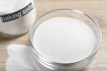Baking soda in glass bowl on wooden table, closeup