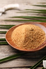 Spoon with coconut sugar and palm leaves on wooden table, closeup