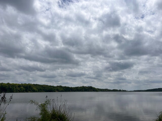 Forest lake on a quiet summer morning, clouds over mountain peaks
