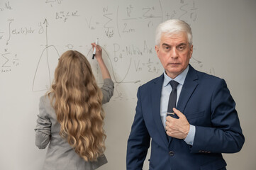 Female student answers a question from an elderly professor at a white board. 