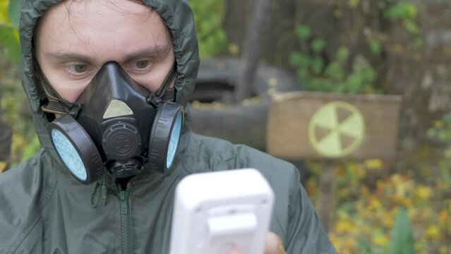 Man in protective suit and mask respirator use radiation geiger counter. Checks level of radiation. Radiation yellow danger sign in radioactive zone. Nuclear weapons, atomic apocalypse concept