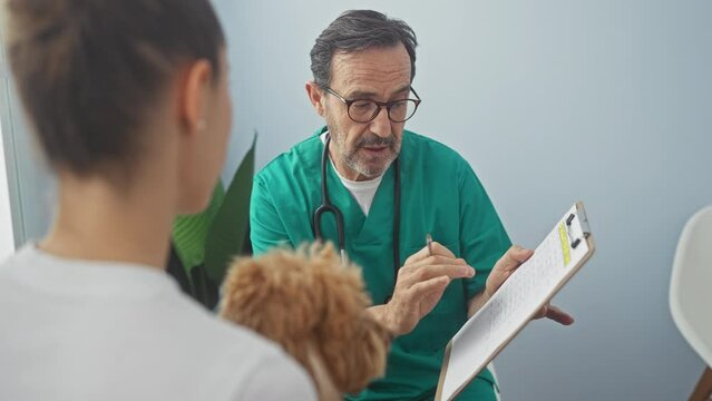 Hispanic veterinarian consults with woman holding poodle in a clinic environment.