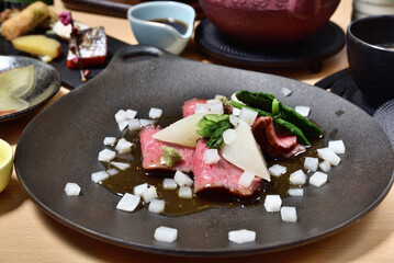 Seared beef salad with fresh vegetables on the black plate. Thinly sliced sashimi style.
