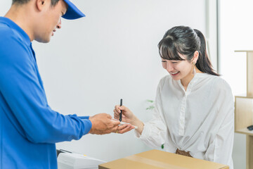 荷物を受け取りスマホにサインをする女性と配達員・配送業の男性
