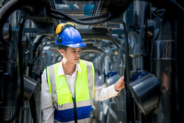 A focused engineer wearing a safety vest and helmet inspects machinery in an industrial setting. The professional diligently checks equipment to ensure proper functionality and safety standards.