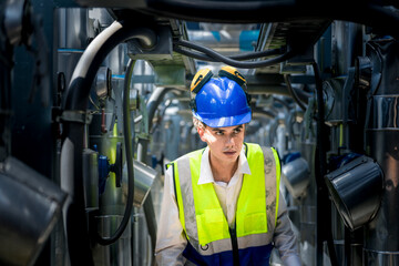 An industrial worker in high-visibility gear and a blue helmet meticulously examines the intricate network of machinery. The engineer is dedicated to maintaining operational efficiency and safety.
