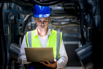 An industrial worker in high-visibility gear and a blue helmet meticulously examines the intricate network of machinery. The engineer is dedicated to maintaining operational efficiency and safety.